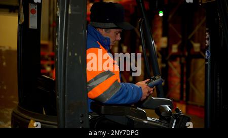 Serbia - Belgrade, August 25, 2022: Side view of a worker in bright uniform sitting inside a lift truck. Creative. Equipment of a warehouse Stock Photo