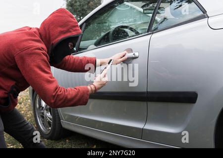 Young fraudster tries to steal someone's car by car link application system in smartphone. Unlocking vehicle using mobile app. Male criminal breaks th Stock Photo