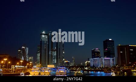View from the river on the night city with skyscrapers and many lights. Action. Ships and yachts flowing along the river at night Stock Photo