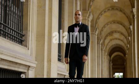 Man in black and white official suit walking in arcuate shaped hall. Action. Man walking outdoors by the building with columns Stock Photo