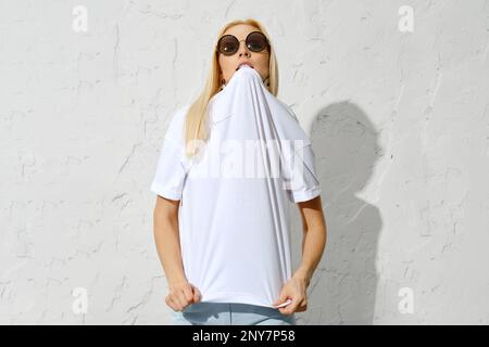 Playful blonde woman bites the collar of a t-shirt Stock Photo