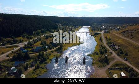 Aerial view of ecological place for living. Clip. Peaceful village with a river and bridge located surrounded by forest Stock Photo