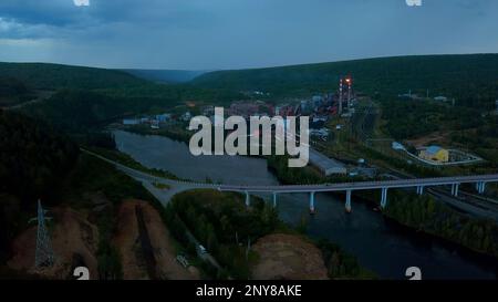 Flying above the river through small town and mountain landscape. Clip. Bridge across the wide river leading to the town Stock Photo