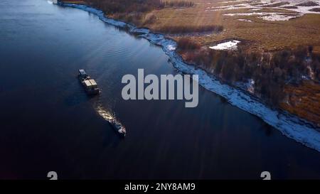 Industrial background with a barge and a river with snowy shore. Clip. Cargo ship transporting goods on a field background Stock Photo