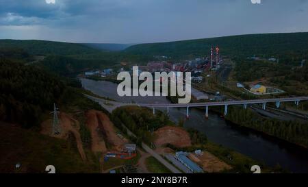 Flying above the river through small town and mountain landscape. Clip. Bridge across the wide river leading to the town Stock Photo