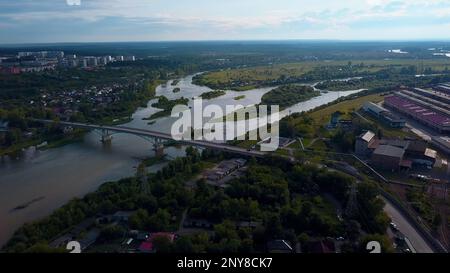 Aerial view of the city parts connected by the bridge. Clip. Wide river flowing along green vegetation and buildings