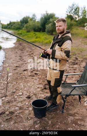 Vertical portrait of confident fisher male holding casting rod standing on  bank waiting for bites on water river at cloudy day, looking at camera  Stock Photo - Alamy