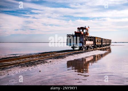 Old train rides on the railway laid in the water through the salt lake. train travels from water. Mined salt in Lake Burlin. Altai. Russia. Bursolith. Stock Photo