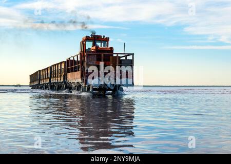 The train floats on the water against the blue sky. Salt industry, salt mining. Stock Photo