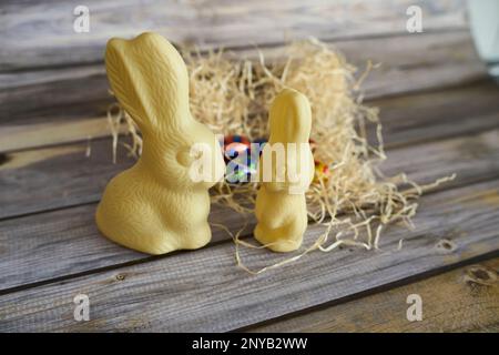 Two white chocolate Easter bunnies atop a pile of hay with chocolate eggs on the background Stock Photo