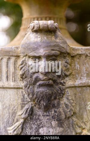 Detail of face on classical urn artwork in garden, Dartington Hall estate gardens, south Devon, England, UK Stock Photo