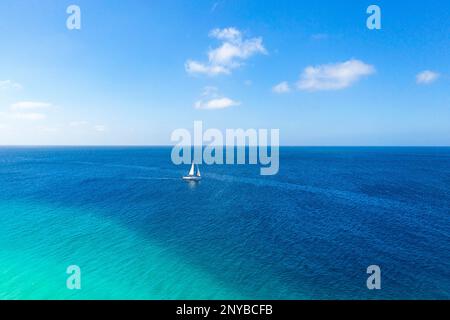 Sailboat with sails on the horizon of the turquoise sea near Sal Island in Cape Verde, surrounded by calm tropical waters and a beautiful seascape. Stock Photo