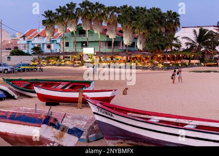 Traditional wooden fishing boats on a sandy beach in Santa Maria town with palm trees and restaurants and hotels at the back, Sal island, Cabo verde Stock Photo