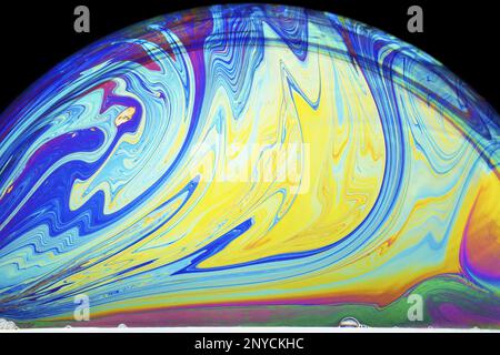 splashes of colorin a soap bubble lit from below against a dark background Stock Photo