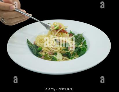 Die cut of Spaghetti Carbonara with fork on white dish on black isolated. Stock Photo