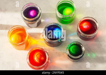 Dyeing Easter Eggs in Colorful Dye in Glass Jars on Marble Counter Stock Photo