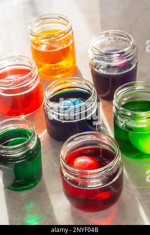 Dyeing Easter Eggs in Colorful Dye in Glass Jars on Marble Counter Stock Photo