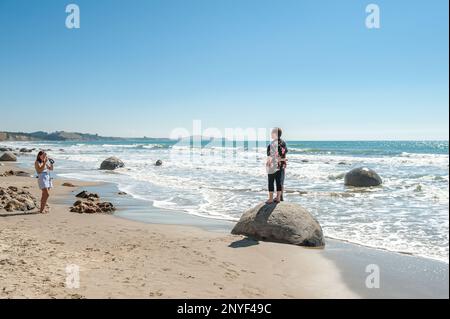 Tourist visit Moeraki boulders in Moeraki. Moeraki boulders are a group of mysterious spherical “stones” on Koekohe Beach. Stock Photo