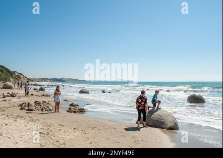 Tourist visit Moeraki boulders in Moeraki. Moeraki boulders are a group of mysterious spherical “stones” on Koekohe Beach. Stock Photo