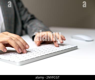 Female hands and wireless computer keyboard on white desk. Stock Photo