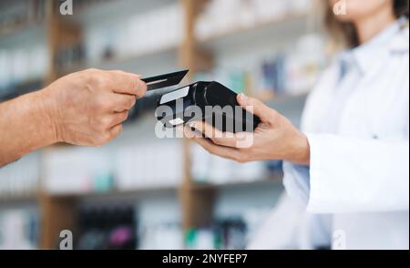 Pharmacist scanning a credit card on a card reader in a chemist. Healthcare worker receiving payment for medication in a drug store. Stock Photo