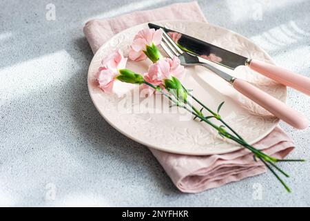 From above table setting with plate and napkin near pink carnation flowers on concrete table Stock Photo