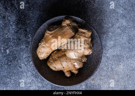 Black stone bowl with ginger roots on concrete kitchen table Stock Photo
