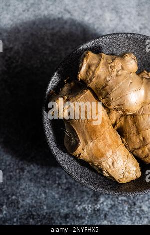 Black stone bowl with ginger roots on concrete kitchen table Stock Photo