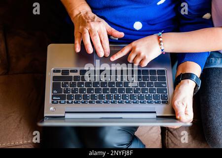 Top view of anonymous senior woman and child surfing internet on laptop while sitting on leather sofa together Stock Photo