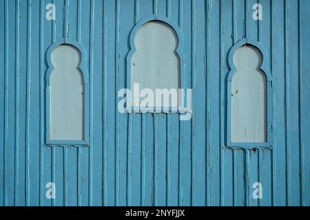 Full frame of blue wooden wall with decorative windows and shabby painted planks on street of Mauritania Stock Photo