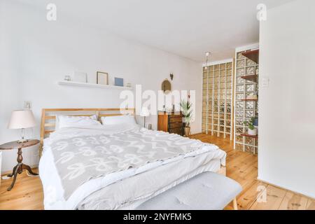 Comfortable cozy bed with pillows and blanket placed near glass door in luxurious sunlit bedroom in wooden floor modern apartment Stock Photo