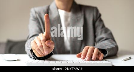 Female person sitting at the desk working on computer touching virtual screen with finger. Stock Photo