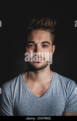 Handsome positive guy with stubble looking at camera while standing on black background Stock Photo