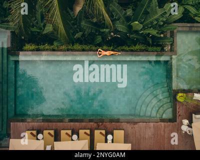 Aerial view of young woman lying on the poolside. Female in bikini ...