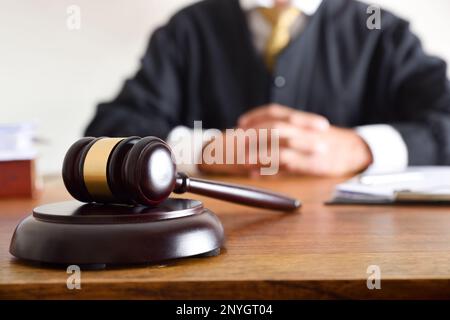 Detail of gavel and judge dressed in the toga sitting in the background on wooden table. Front view Stock Photo