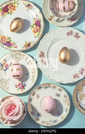 Aesthetic Easter table set up. Vintage dishes, cups and golden eggs on blue background. Easter food and breakfast, pastel colors Stock Photo