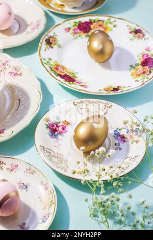 Aesthetic Easter table set up. Vintage dishes, cups and golden eggs on blue background. Easter food and breakfast, pastel colors Stock Photo
