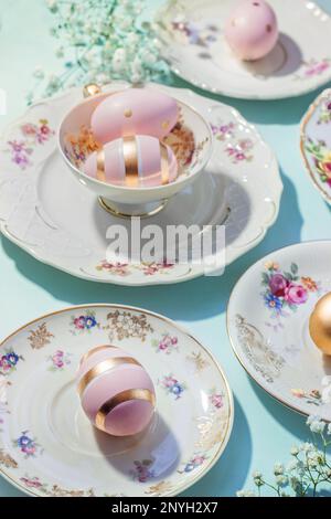 Aesthetic Easter table set up. Vintage dishes, cups and golden eggs on blue background. Easter food and breakfast, pastel colors Stock Photo