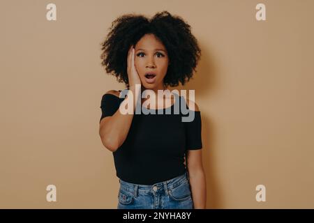 Studio portrait of young shocked african female with unexpected facial expression because of hearing bad news, mixed race woman keeping jaw dropped, w Stock Photo