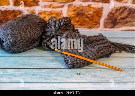 Gray yarn ball and a crochet hook with a started wool hand warmer. Stock Photo