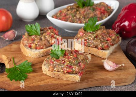 Homemade eggplant caviar with pepper, tomato and garlic on bread toasts on wooden board Stock Photo