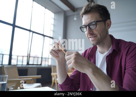 Young focused german man in glasses holding pencil sitting at desk and giving online web lesson or class on laptop computer at home, holding video cal Stock Photo