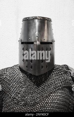 Medieval crusader knight armor, closed iron helmet and chain mail, frontal view  in front of white wall Stock Photo