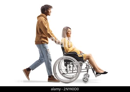 Full length profile shot of an african american man pushing a caucasian pregnant woman in a wheelchair isolated on white background Stock Photo