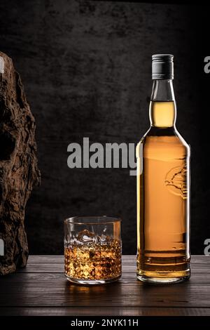 Bottle of whisky and glass with ice on wooden table with dark background with copy space. Vertical format. Stock Photo