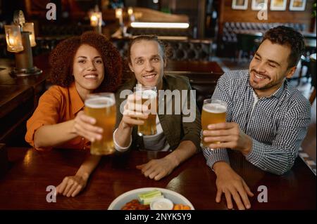 Cheerful friends drinking draft beer at bar table in pub Stock Photo