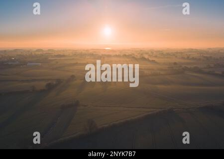 Aerial shot of a sunrise over Schleswig-Holstein, Germany, shot with a Drone, with klong shadows of trees, fog and morning dew Stock Photo