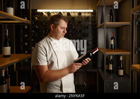 Sommelier expert holding glass bottle choosing wine in cellar Stock Photo