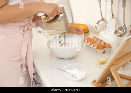 Woman making cake while watching online cooking course via tablet in kitchen, closeup Stock Photo
