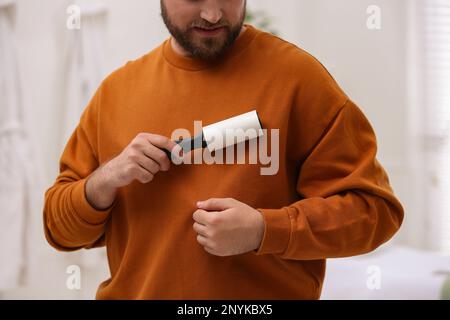 Man cleaning clothes with lint roller at home, closeup Stock Photo